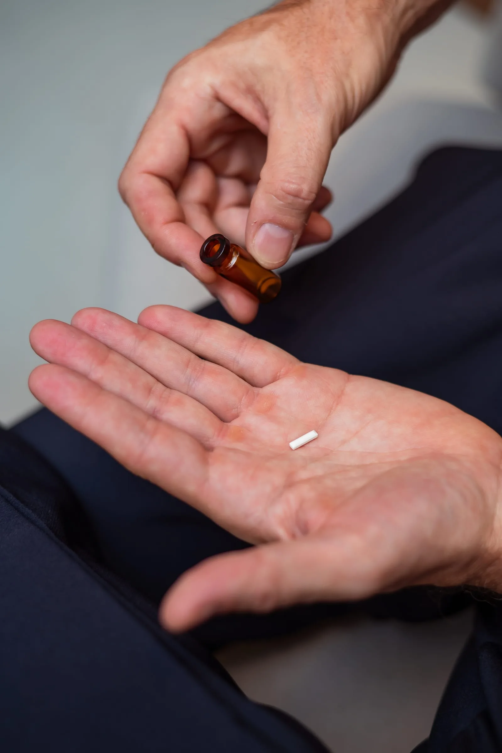 Mãos segurando um implante hormonal absorvível ao lado de um frasco âmbar