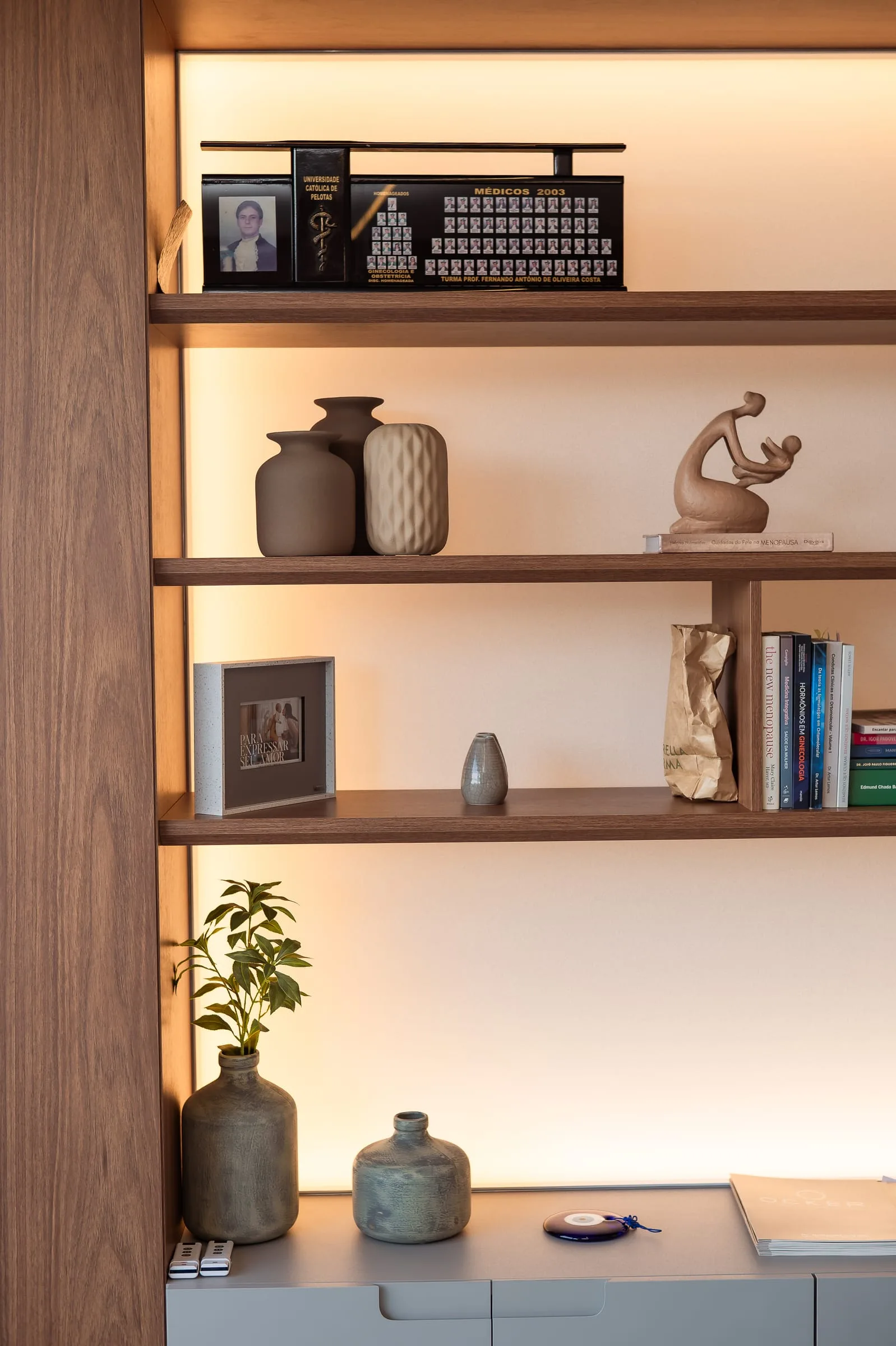 Estante do consultório com escultura de mãe e bebê, cerâmicas e quadro de formatura